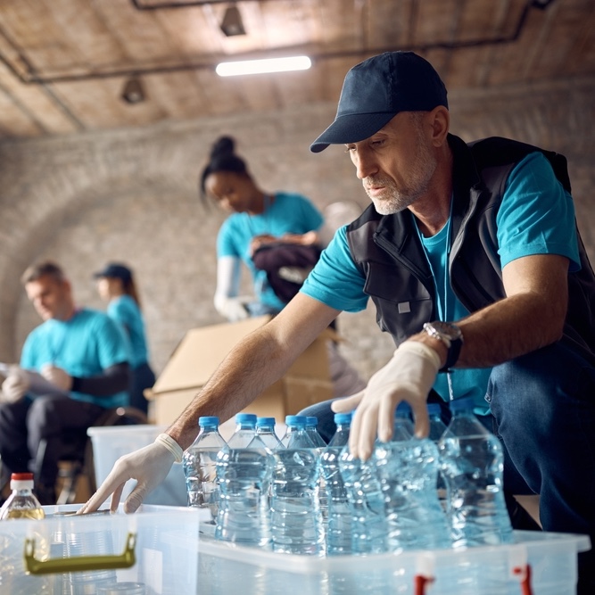 man working as volunteer at community center and arranging donated food and water in boxes